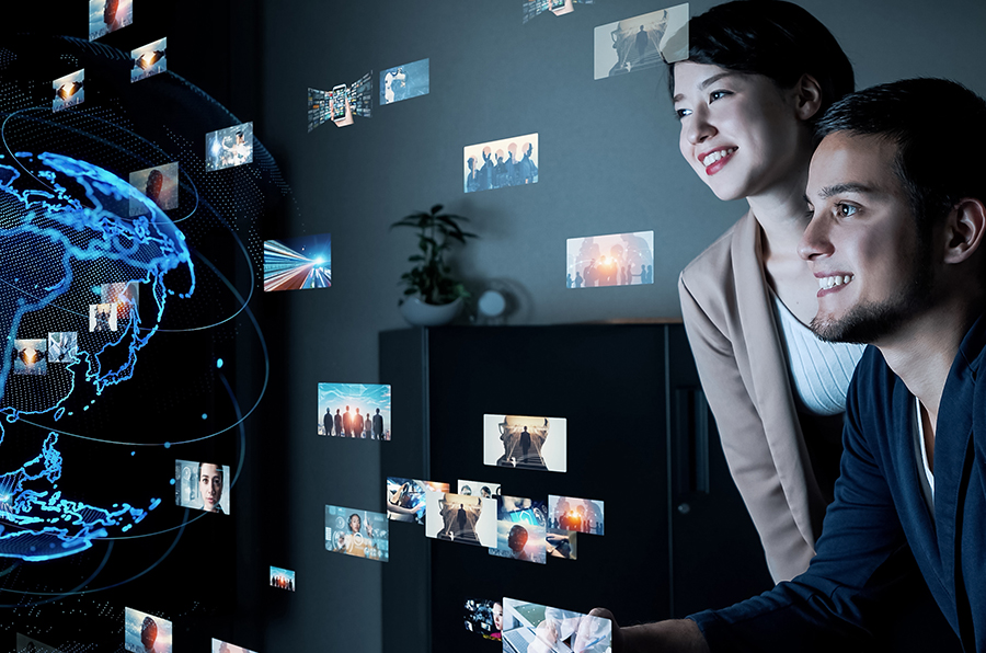 A man and a woman looking at the hologram-like visual representation of Earth with icons hovering above the screen